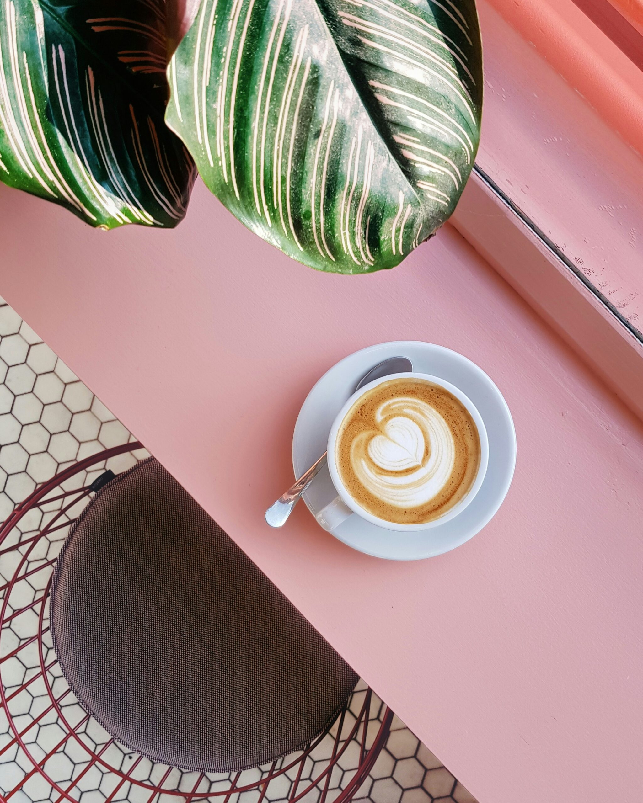 cup of coffee on saucer with teaspoon on pink tabletop